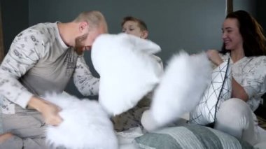 cheerful parents with child in identicals pajamas at a bedroom, family fooling around in bed with pillows