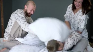 family fooling around in bed with pillows, parents with a child in identicals pajamas at bedroom