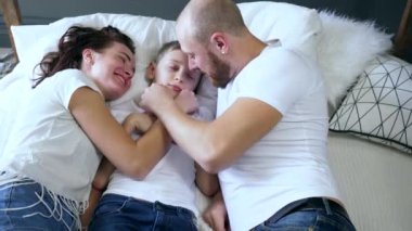mother and father kisses the son on bed closeup indoors, lovely family moments