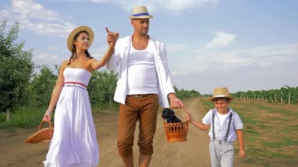 Happy village family on nature, mother, father and child goes with little dog in basket on country road — Wideo stockowe