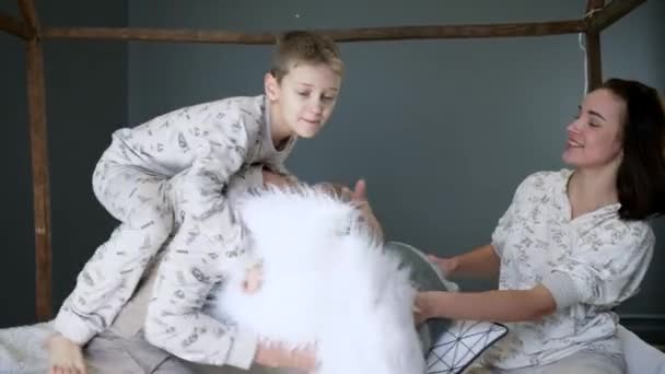 Happy family in identical pajamas beat each other with pillows on the bed close-up in studio on photoshoot — Stock video