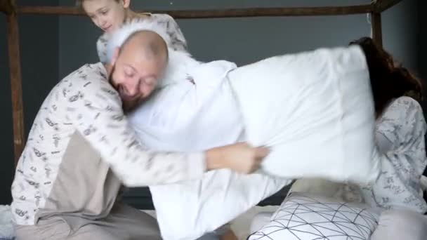 Pajamas party, son with their parents in identical pajamas beat each other with pillows on bed — Stockvideo