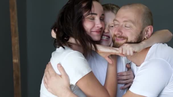 Boy hugs his young parents close up, family have fun together in studio on photo shoot — Stockvideo