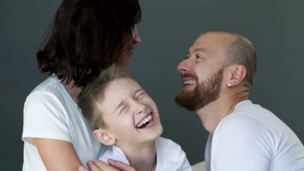 Happy family in identical white T-shirts hugs each other close up in studio on photo shoot — Stock video