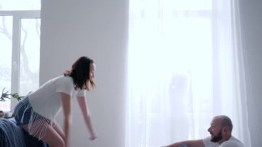 husband catches wife and then hugs her on bed on background of dancing son behind the curtains at home