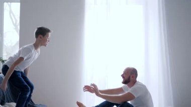 young father catches son and then tickles him on bed and have fun playing at home, slow motion