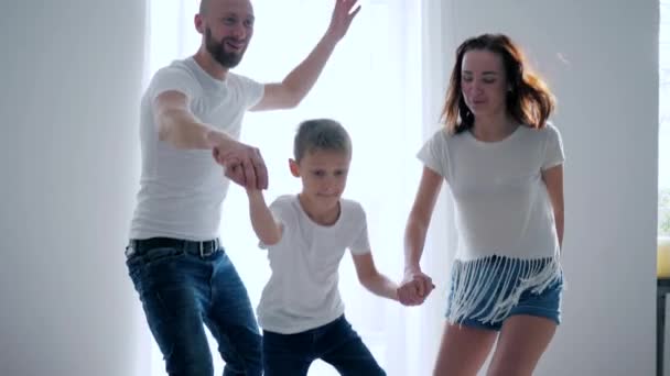 Mom, dad and son in identical white T-shirts together fun jumping on bed, happy moments — Stockvideo