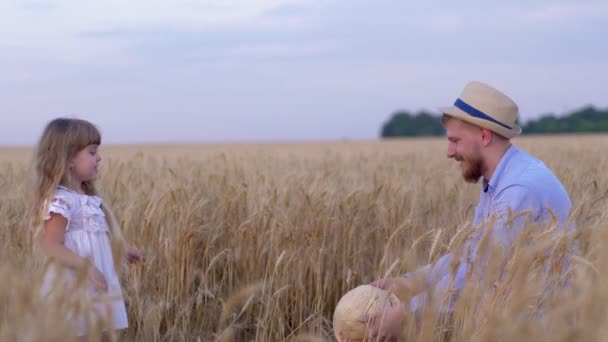 rodinný venkovský víkend, mladý pohledný táta a jeho holčička hraje, zatímco on ukazuje triky se slamákem házení na sebe v sklizni sezónní obilí pšenice pole