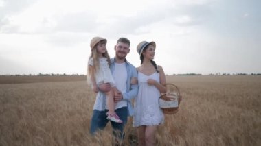 Mutlu bir aile ve küçük bir kız çocuğu sonbahar tarlasında sarı buğday başaklarında yürüyüp konuşuyorlar sepetteki ekmekle.