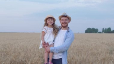 Mutlu baba ve kızın portresi, neşeli baba, güler yüzlü çocuk kızla birlikte elinde hasadı olan altın buğday tarlasında sonbahar zamanı kalır.