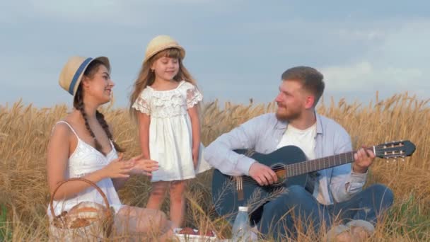 Fröhliche Familienausflüge, der Vater spielt Saiteninstrument, während die Mutter in die Hände klatscht und die kleine Tochter im Brotfeld tanzt — Stockvideo