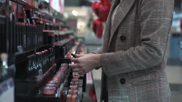 Primeros planos, chica está probando lápiz labial para poner a la mano durante una venta en la tienda de cosméticos, maquillaje — Vídeo de stock