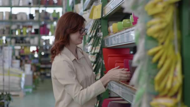 Niedlich lächelnde Frau mit Brille kauft farbige Blumentöpfe für heimische Pflanzen im Kaufhaus für Gärtner, Designkonzept — Stockvideo