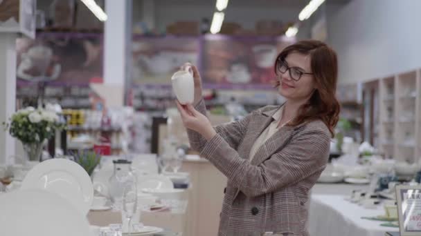 Mooie shopper met bril voor vrouwelijk zicht kiest servies voor set van gerechten in warenhuis met huishoudelijke artikelen, design concept — Stockvideo