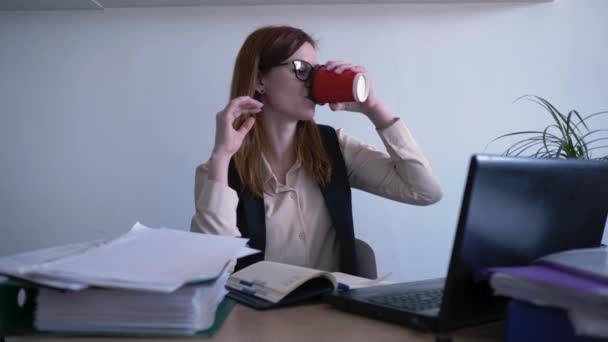 Moe overwerkte jonge vrouw drinkt koffie en voelt zich moe, hoofdpijn van vermoeide ogen na het werken op de computer neemt af bril, kantoor werkdag — Stockvideo