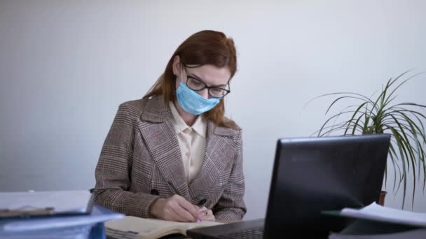 Gesundheitsschutz, junge Büroangestellte in medizinischer Schutzmaske arbeitet in Quarantäne und benutzt ein Antiseptikum, um ihre Mobiltelefone zu desinfizieren, Pandemie — Stockvideo