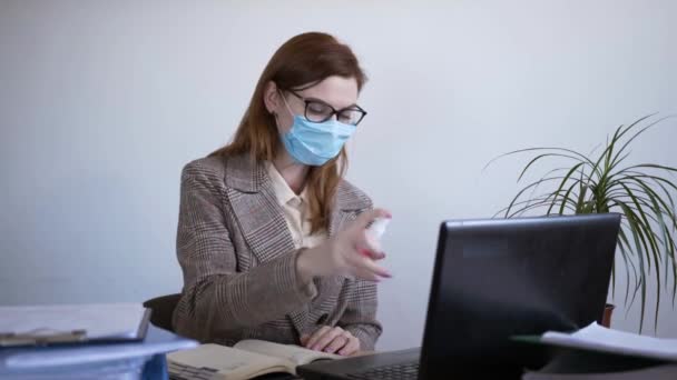 Pandemia coronavirus, joven empresaria en mascarilla médica utiliza un antiséptico para prevenir virus e infecciones, desinfección de teléfonos inteligentes y teclado portátil, cuarentena — Vídeo de stock