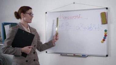 Eğitimli çocuklar, genç bir kadın gözlüklü bir matematik öğretmeni öğrencilere ders sırasında beyaz bir manyetik tahtaya yazılan formülü anlatıyor.
