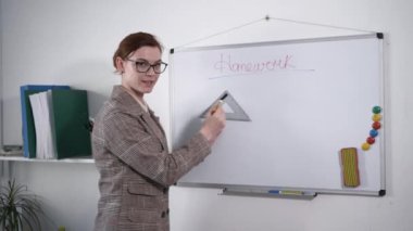 Gözlüklü bayan öğretmen, ilkokul öğrencilerine sınıf ve okulda ders sırasında ev ödevlerini anlatıyor.
