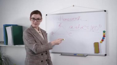 Eğitim konsepti, gözlüklü güzel öğretmen derste üçgenin geometrik şeklinden bahsediyor, genç kadın manyetik panonun arka planındaki anaokulu ödevini anlatıyor