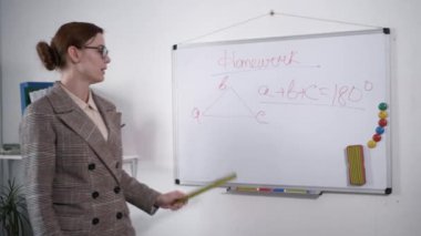 Okul çocukları eğitimi, elinde cetvel olan genç bayan öğretmen beyaz manyetik tahtaya karşı ders sırasında çocuklara ev ödevlerini açıklıyor