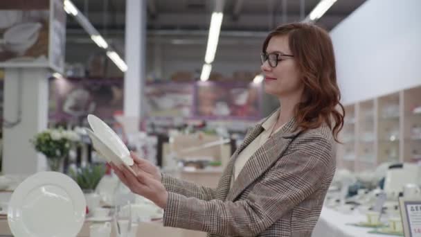 Venta, chica atractiva en gafas para la vista elige nuevos platos para el servicio en la ferretería — Vídeos de Stock