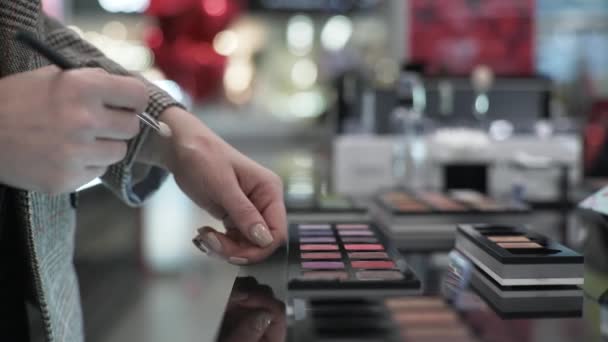 Руки покупателя крупным планом, женщина с кистью в руках тестирует косметику макияжа в магазине, продажа — стоковое видео