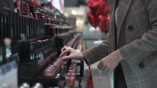 Comprador feminino examina produtos de maquiagem, menina examina batons na loja de cosméticos — Vídeo de Stock
