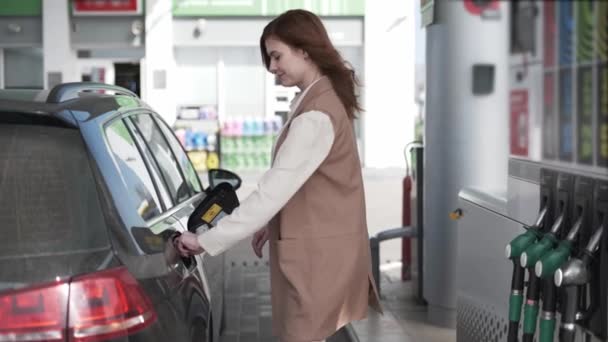 Young female customer fueling car with gasoline at gas station, girl inserts fuel nozzle is getting inserted into automobiles tank, paying — Stock Video