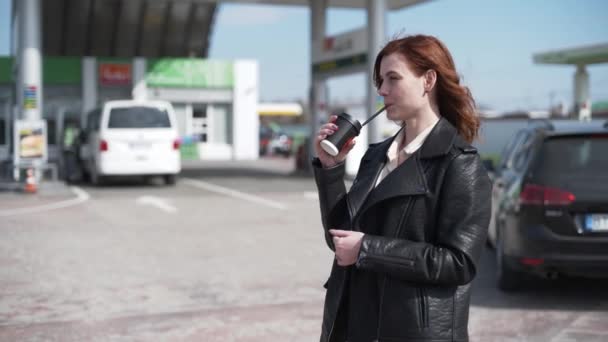 顾客关怀，快乐的女孩顾客对顾客服务感到满意，在加油站加油的时候喝着外卖的咖啡，汽油的价格 — 图库视频影像