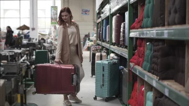Giovane attraente acquirente femminile scegliere una valigia da viaggio a ruote in un negozio di viaggi per vacanze, commercio — Video Stock