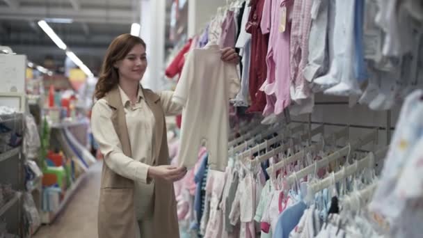 ショッピングセンターお母さんはスーパーで子供服の棚の近くの子供のための服を選ぶ女性の親は衣料品店で子供のための下着を買う — ストック動画