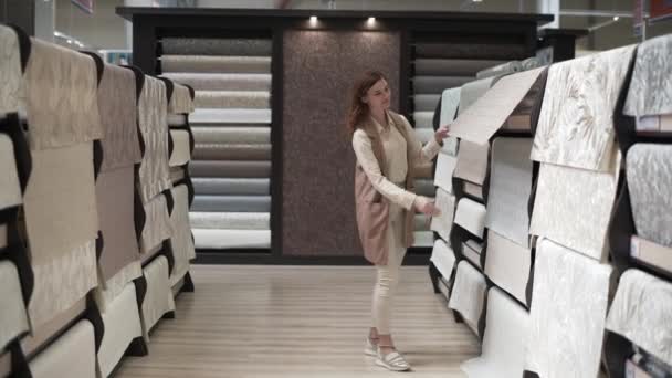 魅力的な女性の買い物客のデザイナーは、ペーパーハンギングと棚の背景にあるアパートの改装ハードウェア店のための新しい壁紙を選択 — ストック動画