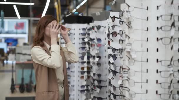 Zakupy, młoda stylowa dziewczyna kupująca wybiera okulary przeciwsłoneczne w centrum handlowym podczas sezonowej sprzedaży, styl życia — Wideo stockowe