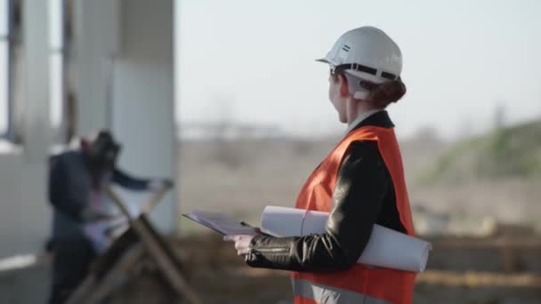 Mosolygós professzionális női nehézipari mérnök sisak háttér egy építési terület hangár, ahol hegesztési szikrák repülnek — Stock videók