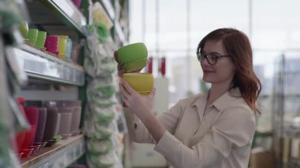 Heureux acheteur féminin avec des lunettes pour la vision choisit des pots de créateurs pour les plantes à la maison pour décorer l'intérieur de la maison ou le bureau dans le magasin de fleurs — Video