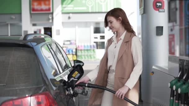 Gas prices, girl fueling car with gasoline at gas station, girl inserts fuel nozzle is getting inserted into automobiles tank at gas station — Stock Video