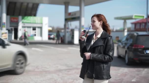 Presupuesto, conductor femenino está satisfecho con el precio de la gasolina y disfruta de servicio tiene café en las manos y muestra el pulgar hacia arriba, mientras que el coche de repostaje en la gasolinera — Vídeo de stock