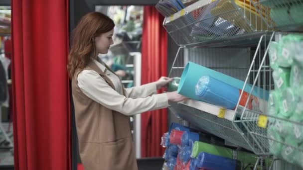 Mignon femme shopper ouvre tapis de yoga dans le supermarché, fille mène un mode de vie sain et se prépare pour la leçon de yoga ou de méditation à la maison ou en studio — Video