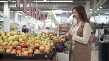 Yaşam tarzı, elinde yemek sepeti olan mutlu kadın alışverişçisi süpermarketten taze elma meyvesi topluyor, ticaret yapıyor.