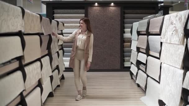Attractive female customer buys goods for home renovation in hardware store, woman chooses new wallpaper for room decoration on background of shelves with paperhanging — Stock Video
