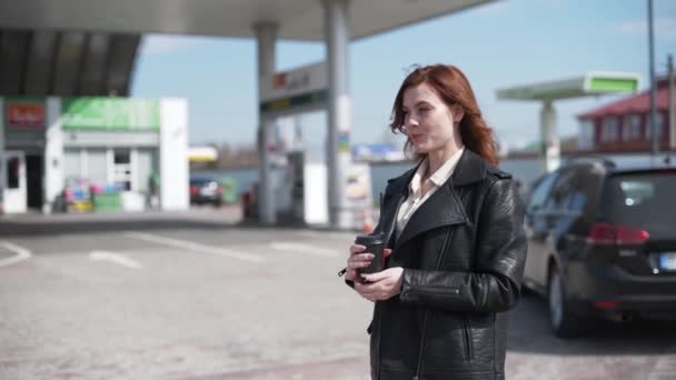 Szerviz, elégedett női ügyfél iszik kávét egy benzinkút, míg az autó tankolnak, üzemanyag árak — Stock videók