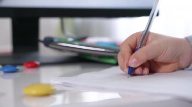 Yakın plan çekimde, çocuk evde çocuklara ders vermek için masa başında kalemle ödev yazıyor.