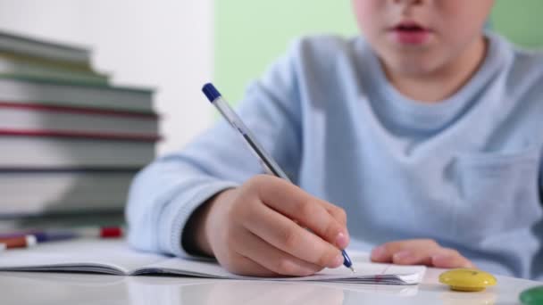 Kleiner Junge schreibt Hausaufgaben in Notizbuch, männliches Kind unterrichtet zu Hause am Tisch sitzend, Nahaufnahme — Stockvideo
