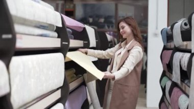 Kadın alıcı, apartman raflarındaki duvar kağıtlarını onarım için alıyor, gülümsüyor ve el, dekor ve tasarım ile sınıfı gösteriyor.