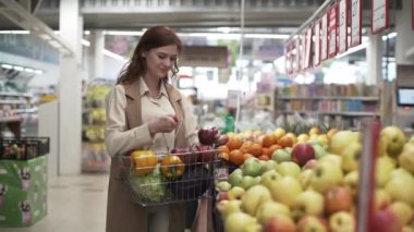 Perakende mağazası, elinde yemek sepeti olan çekici, güler yüzlü kadın alışverişçi pazar yerinden taze meyve topluyor.