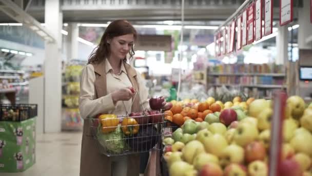 Tienda al por menor, atractivo comprador femenino sonriente con canasta de alimentos en las manos recoge frutas frescas en el mercado — Vídeos de Stock
