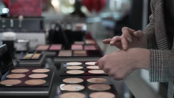 Belas mãos femininas close-up, menina está testando cosméticos decorativos na loja moderna, aplique pó na mão para escolher o tom de pele — Vídeo de Stock