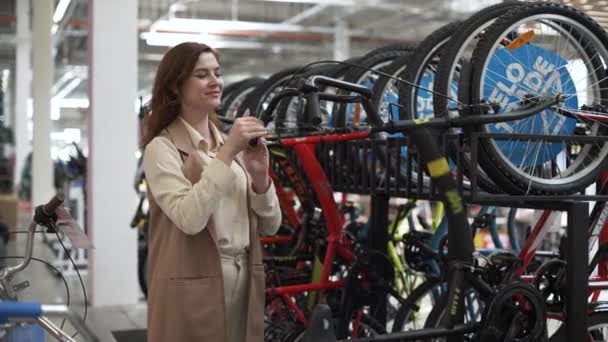 Красивая богатая женщина-покупатель, которая любит здоровый образ жизни выбирает велосипед для езды на велосипеде во время продажи в спортивном магазине, покупки — стоковое видео