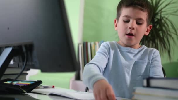 Treinamento remoto, um menino inteligente aprende lições em casa sentado em um computador e assiste a uma aula de vídeo com seu professor em uma tela do monitor — Vídeo de Stock